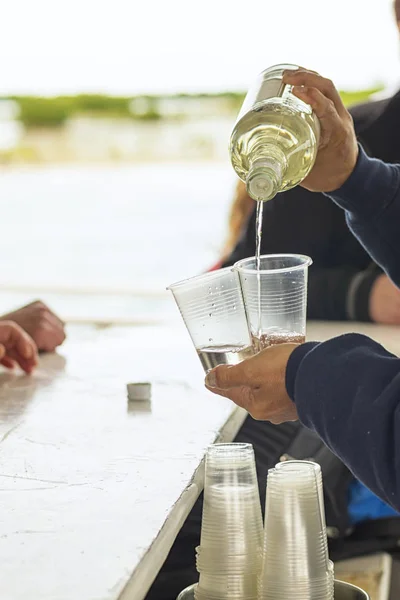 The barman from a bottle pours alcohol into single plastic cups — Stock Photo, Image