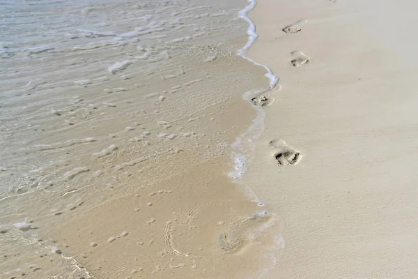 Ola de mar con espuma corre a la orilla arenosa y se lleva los pies — Foto de Stock