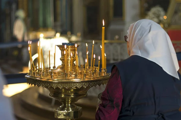An old woman puts a candle in front of an icon