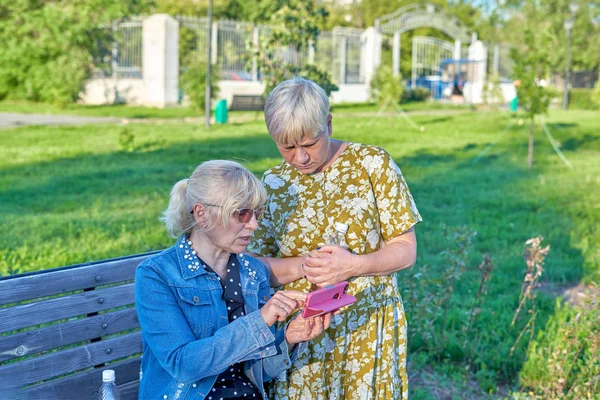 Two old women looking at a smartphone in the Park summer day