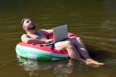 Dizüstü bilgisayarı olan genç serbest çalışan suda güneşleniyor.