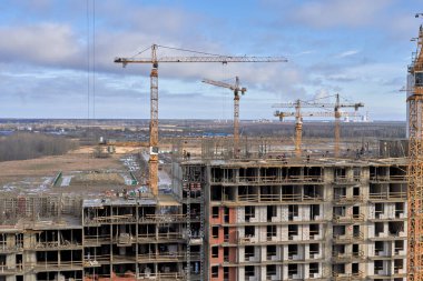 Bir yerleşim alanı kompleksi ve kule vinç inşaatı. İnşaat halindeki bir evin en üst katında miğfer ve maske takan bir sürü inşaatçı var.
