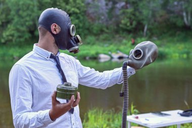 Gaz maskeli çocuk gaz maskeli adam nehir ve ormanlı doğal manzaranın arka planına karşı kol mesafesini koruyor.