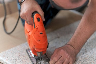 Lavabo için tezgahta bir delik açmak, evde mobilya montajı. Elektrikli yapboz elinde, yakın plan..