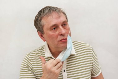 50 yaşında, yorgun yüzlü ve ıslak gözlü bir adam. Kişiden tıbbi bir maske çıkarın. Açık arkaplanda bir portre