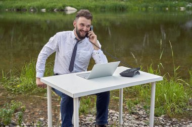 Ofis masasında, gölün arka planında telefonla gülümseyen genç hippi. Dünyanın herhangi bir yerinden destek