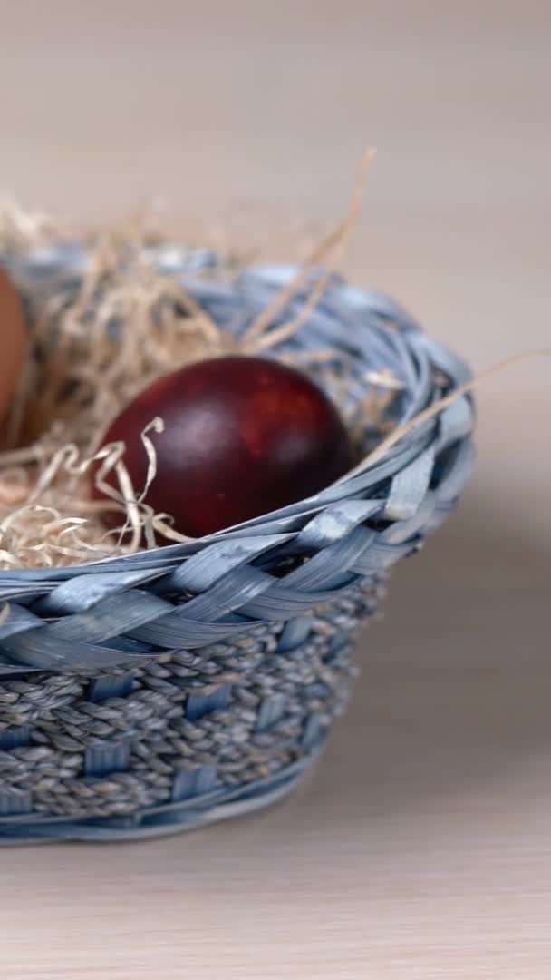 Huevos de color Pascua que yacen en la hierba seca en la canasta azul. Disparo vertical — Vídeos de Stock