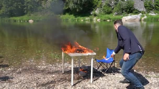 En kontorist bränner en arbetsplats vid floden. Möblerna i branden — Stockvideo