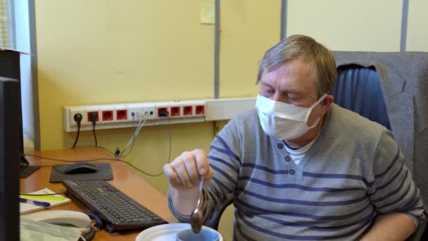 Офисный работник пытается пить чай на рабочем месте без снятия медицинской маски — стоковое видео
