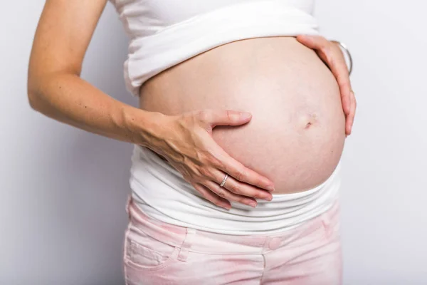 Gravid kvinde kærtegner hendes mave over hvid baggrund - Stock-foto