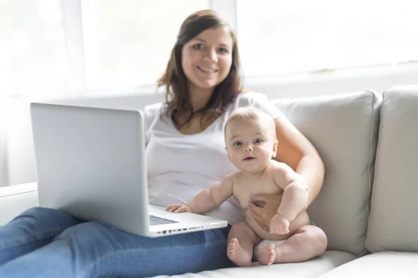 Mor och baby barn funderar på att spela och läsa dator på soffan hemma — Stockfoto