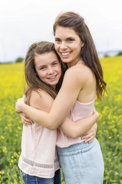 Glückliche Familie Mutter und Kind Tochter Umarmung auf gelben Blumen in der Natur im Sommer — Stockfoto