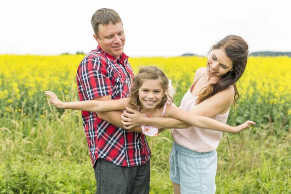 Glückliches Familienpaar nd kleine Tochter auf gelben Blumen in der Natur im Sommer — Stockfoto