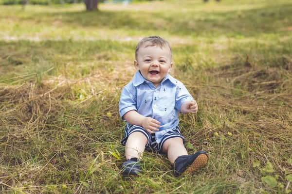 Lycka pojke sitter på gräset i fältet — Stockfoto