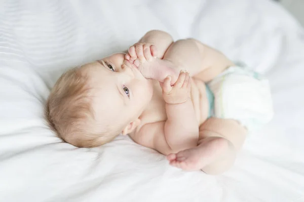 Cute happy 7 month baby girl in diaper lying and playing — Stock Photo, Image