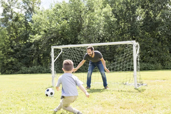Młody ojciec z synkiem grający w piłkę nożną na boisku — Zdjęcie stockowe