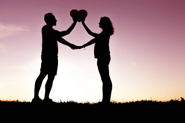 Romántica pareja joven sosteniendo la forma del corazón en las manos al atardecer —  Fotos de Stock