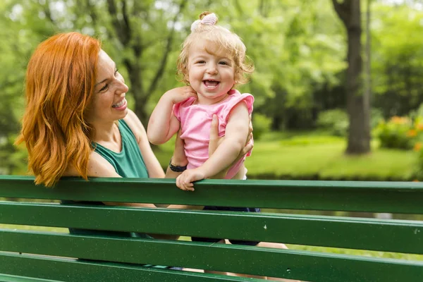 Mother and her little daughter sitting on a park bench — Stock Photo, Image