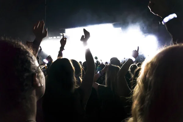 Silhuetas de multidão de concerto na frente de luzes de palco brilhantes. Fundo escuro, fumaça, holofotes de concerto — Fotografia de Stock