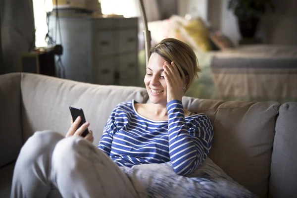 女人坐在沙发上休息和好用的手机 — 图库照片