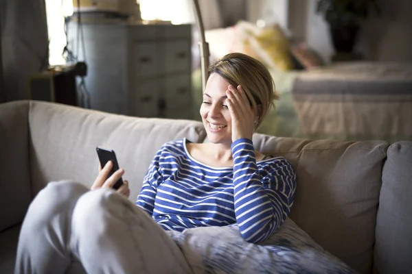 Nő ül a kanapén, hogy egy jó ideje a mobiltelefon — Stock Fotó