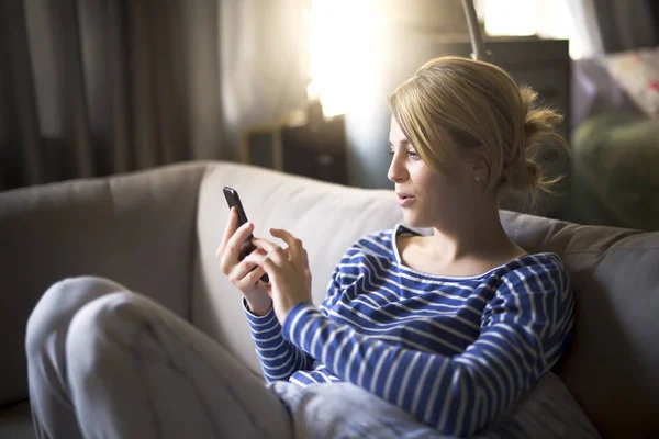 Mujer sentada en el sofá pasar un buen rato con el teléfono celular —  Fotos de Stock