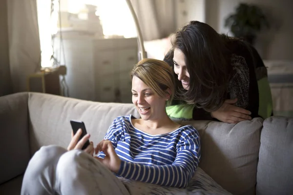 People relations. Two girls are speaking and using cellphone on sofa — Stock Photo, Image