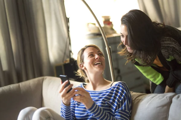 Relations humaines. Deux filles parlent et utilisent un téléphone portable sur le canapé — Photo
