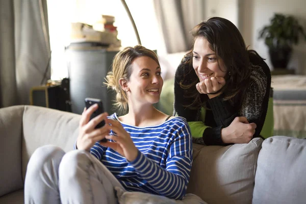 Relations humaines. Deux filles parlent et utilisent un téléphone portable sur le canapé — Photo