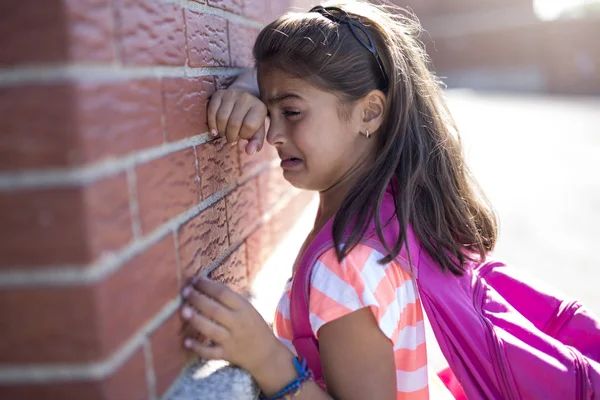 Seks år gammel skole pige græde ved siden af mursten væg - Stock-foto