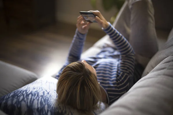 Mujer sentada en el sofá pasar un buen rato con el teléfono celular —  Fotos de Stock