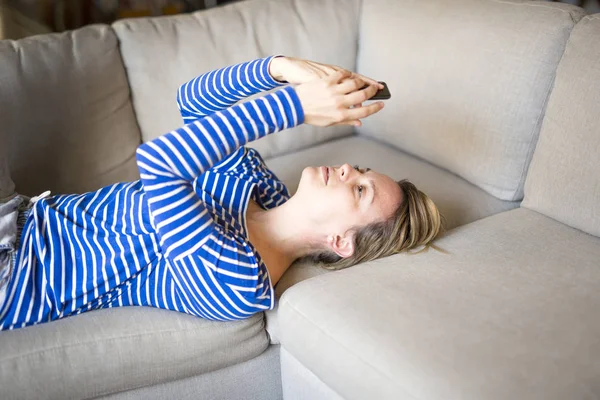 Mulher sentada no sofá tomar algum bom tempo com celular — Fotografia de Stock