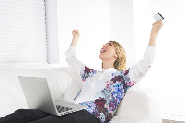 Prachtige blonde vrouw rusten op een witte Bank thuis en met behulp van een laptop — Stockfoto