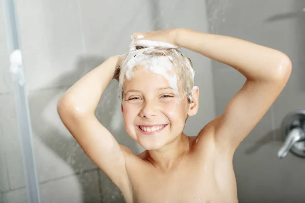 Счастливый мальчик моет голову в душе в ванной комнате — стоковое фото