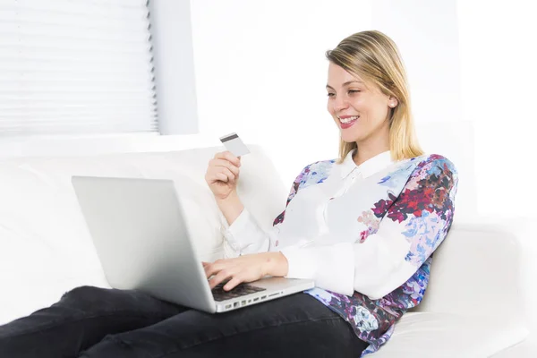 华丽的金发碧眼女人在家白色的沙发上休息，使用一台笔记本电脑 — 图库照片