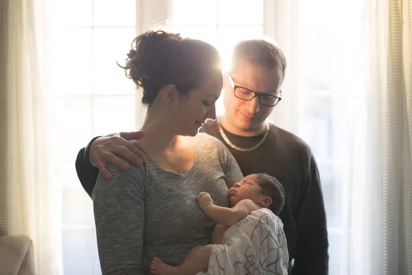 Família feliz, mãe e pai brincando com o bebê em casa perto da janela — Fotografia de Stock