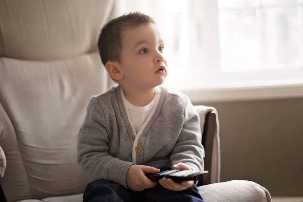 Malý chlapec je sledování televize, zatímco sedí na gauči — Stock fotografie