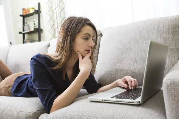 Casual jonge vrouw liggend op de Bank en met behulp van laptop thuis — Stockfoto