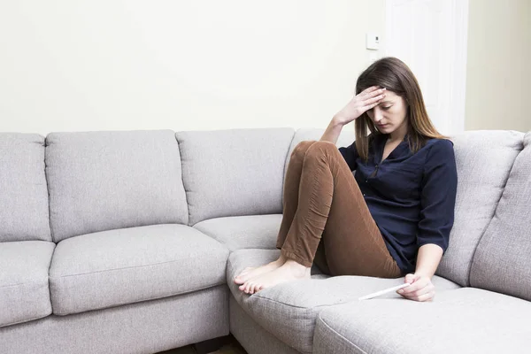 Ragazza seduta su un divano a casa mentre legge i risultati del suo recente test di gravidanza — Foto Stock