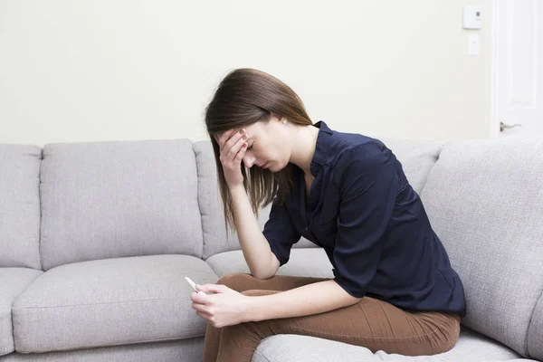 Girl sitting on a couch at home while reading the results of her recent pregnancy test — Stock Photo, Image
