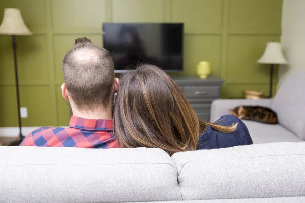 Όμορφο ζευγάρι βλέποντας τηλεόραση καθισμένος στον καναπέ στο σπίτι — Φωτογραφία Αρχείου