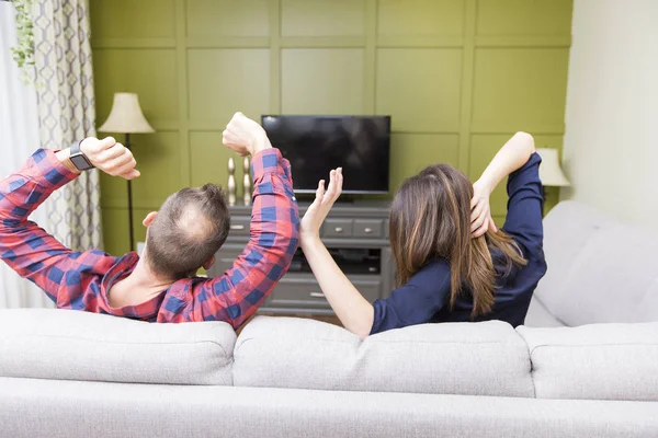 Beautiful couple watching TV sitting on couch at home — Stock Photo, Image