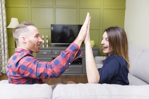 Beautiful couple watching TV sitting on couch at home — Stock Photo, Image