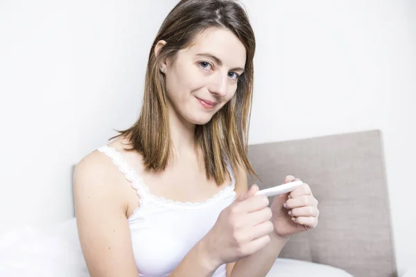 Ung kvinna i sovrum hemma klädd i vit kontrollera gravid test — Stockfoto