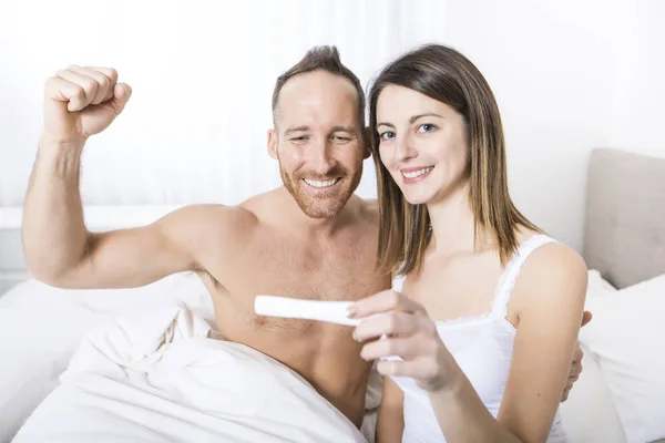 Веселая пара узнаёт результаты теста на беременность сидя на кровати — стоковое фото