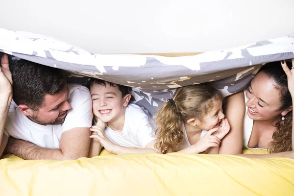 家族、子どもと家庭のコンセプト - 自宅の毛布の下の 2 人の子供と幸せな家庭 — ストック写真