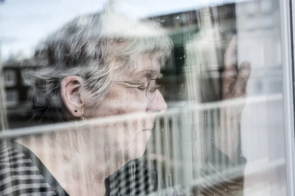 Senior woman looking out through a window like depress — Stock Photo, Image