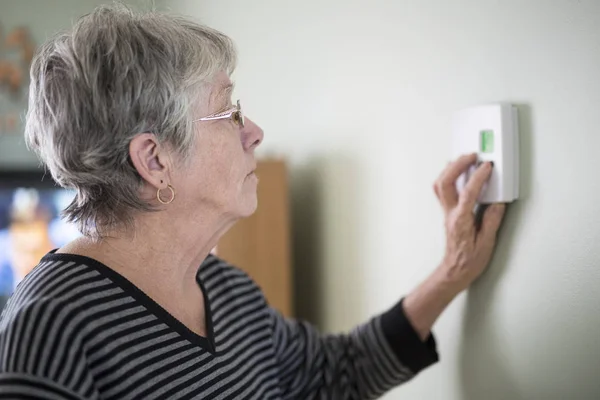 Старшая женщина регулирует свой термостат — стоковое фото