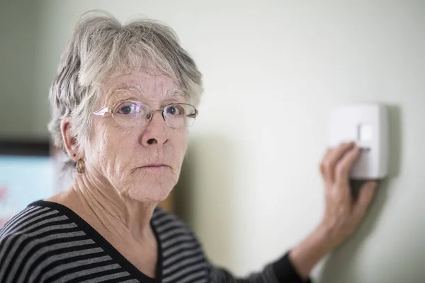 Senior mulher ajustando seu termostato — Fotografia de Stock
