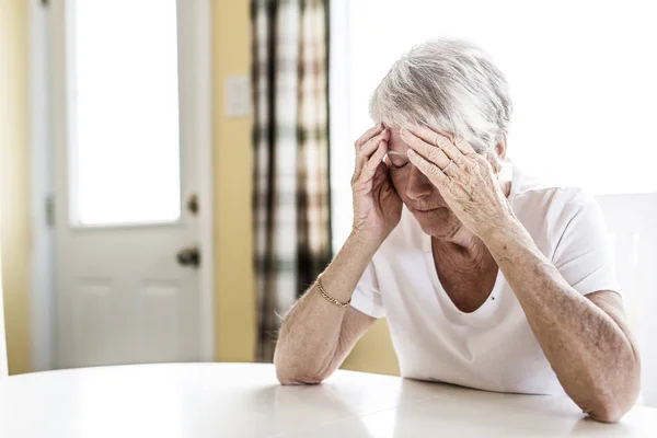 Mujer madura en casa tocándose la cabeza con las manos mientras tiene dolor de cabeza —  Fotos de Stock
